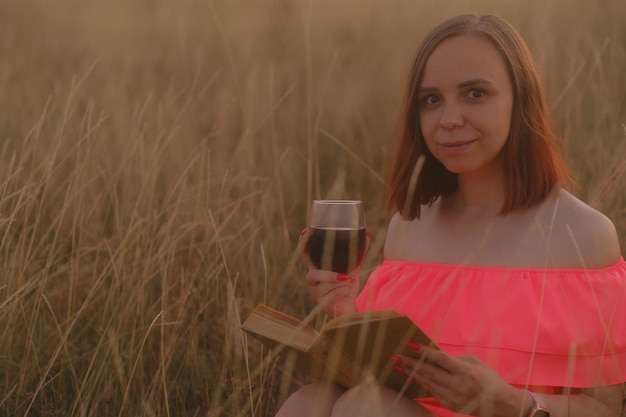 Smiling lady reading book and drinking wine in field