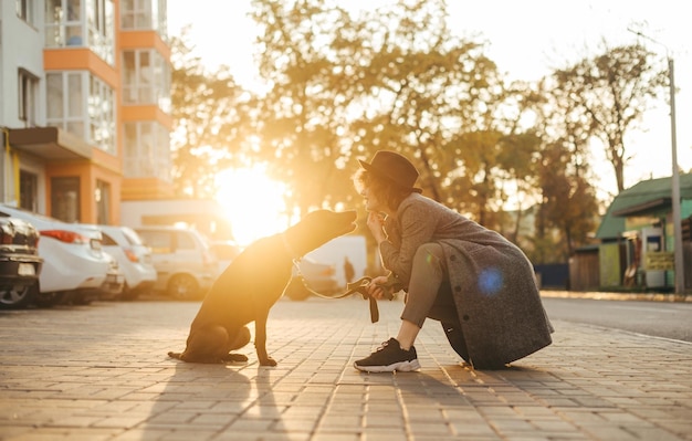 Smiling lady sits with dog on leash against sunset background and talks Pets concept