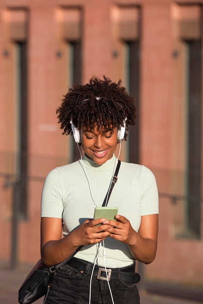 Smiling latin american woman with headphones listens to music on smartphone