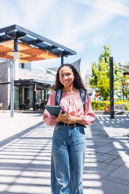 Smiling latin university student woman standing and holding her books outside of the campus