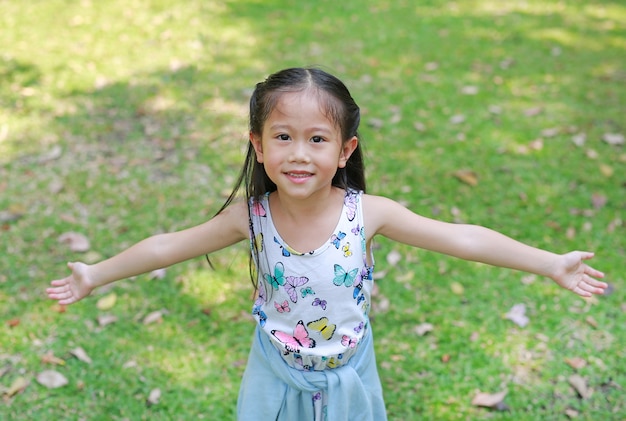 Smiling little Asian child girl opened her hands in the summer garden.