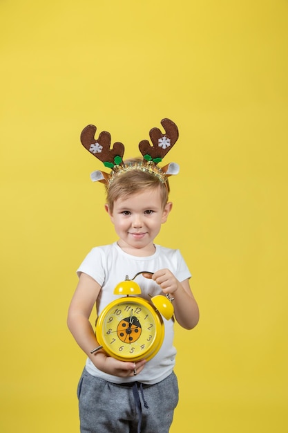 A smiling little boy in in christmas reindeer costume with alarm clock