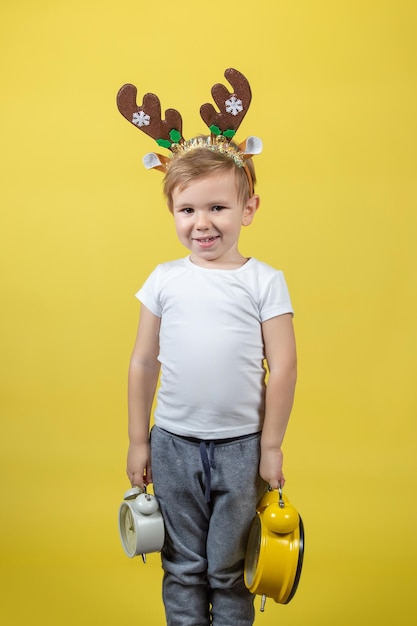 A smiling little boy in in christmas reindeer costume with two alarm clocks