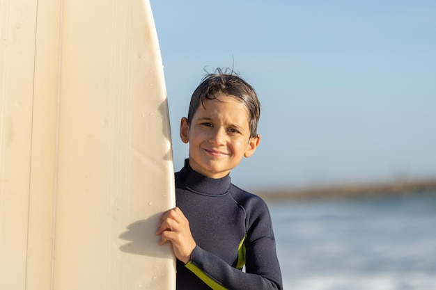 Photo smiling little boy peeking out from behind a surfboard