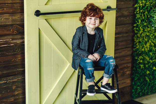 Smiling little boy in ripped jeans sitting on ladder and looking relaxed