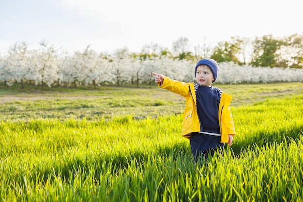 A smiling little boy in a yellow jacket runs through a blooming garden Happy childhood