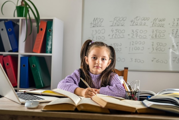 Smiling little Caucasian girl having video call in distance classroom with teacher using laptop happy little child excited greeting with tutor studies online on a computer home schooling concept