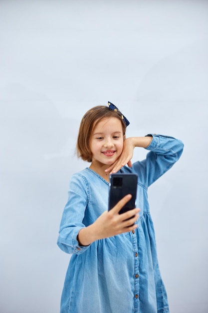 Smiling little girl in casual denim dress hold smartphone do selfie