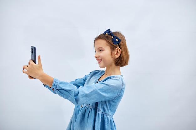 Smiling little girl in casual denim dress hold smartphone do selfie