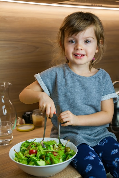 Smiling little girl cooking simple green vegetable salad.