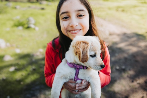 Smiling little girl embracing a golden retriever puppy in the park