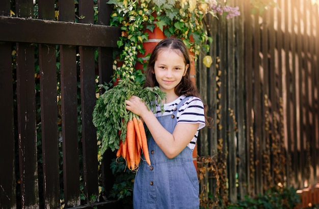 Smiling little girl in a garden holds a bunch of fresh carrots