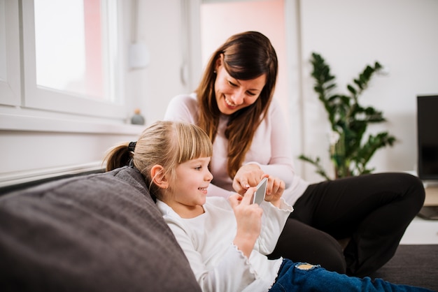 Photo smiling little girl and her mother using smartphone.