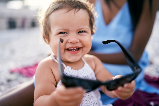 Smiling little girl holding big sunglasses in her hands