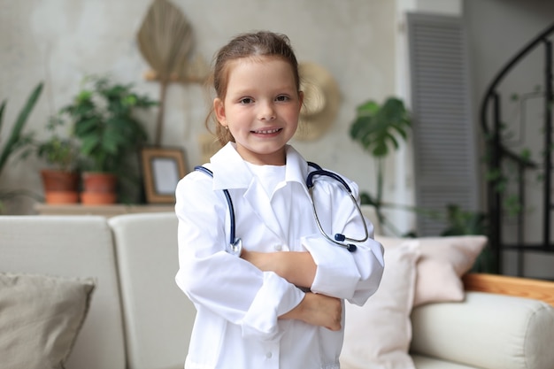 Smiling little girl in medical uniform playing with stethoscope at home.