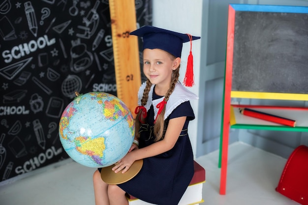 Smiling little girl in a school uniform and pigtails holding globe in classroom.