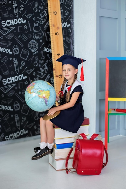 Smiling little girl in a school uniform and pigtails holding globe in classroom.