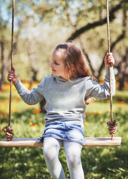 Smiling little girl sitting on a swing in the garden