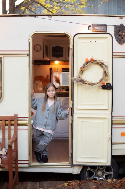 Smiling little girl standing  near trailer door porch RV house in garden