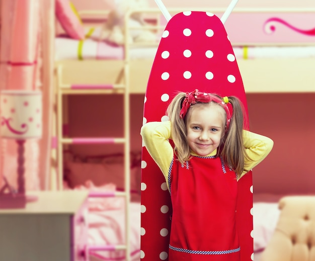 Smiling little girl stands in front of ironing board