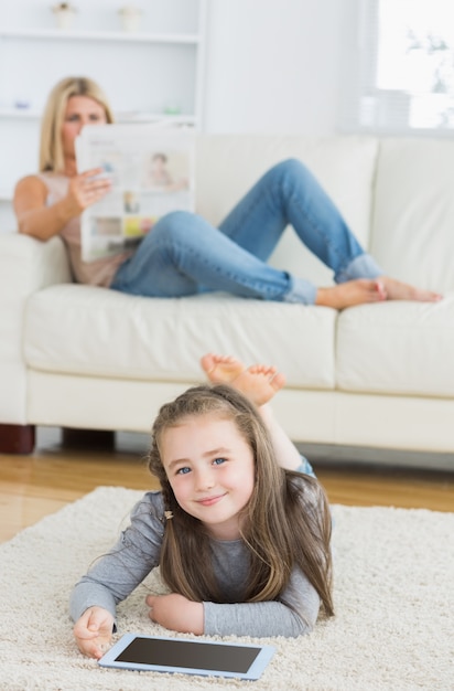 Smiling little girl using tablet while her mother is reading newspaper