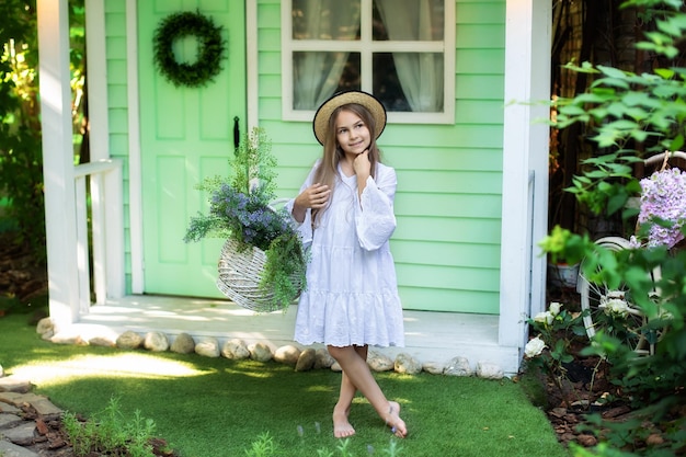 Smiling Little girl in white dress and hat with basket wildflowers on green lawn in garden