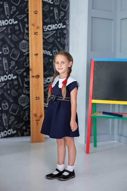 Smiling Little girl with pigtails and in a school uniform stands classroom at school