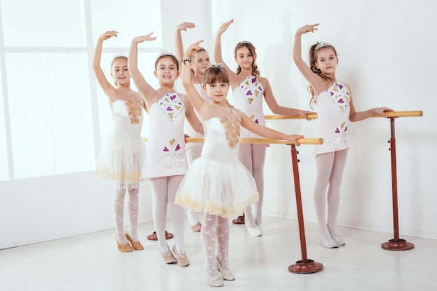 Smiling little girls using barre while practicing in dance studio. Looking at camera.