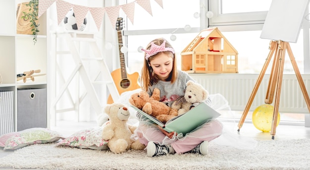 Smiling little princess reading for teddy bears indoors