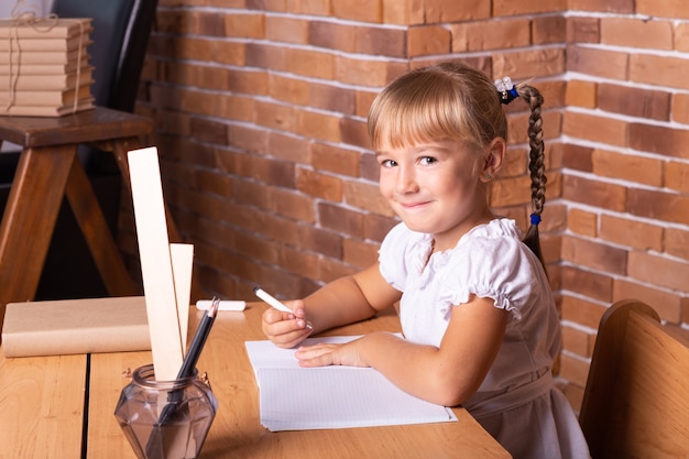 Smiling little student girl sitting at a school desk. The child is doing homework. Preschool education.