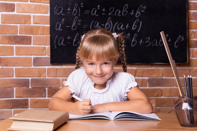 Smiling little student girl sitting at a school desk and studying math