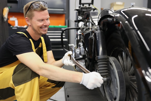 Smiling locksmith with wrench near motorcycle wheel in car workshop motorcycle warranty service