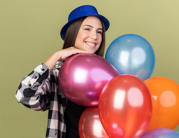 Smiling looking side young beautiful girl wearing blue hat holding balloons 