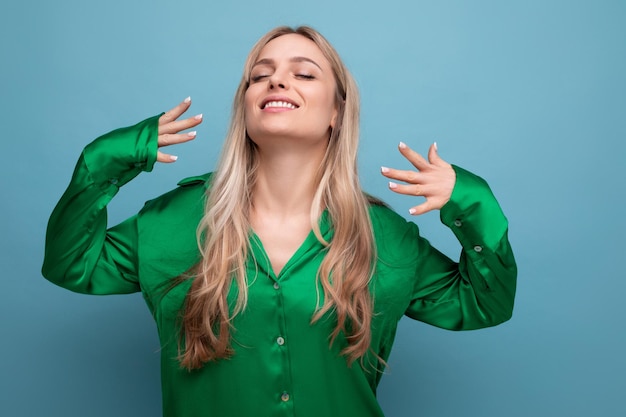 Smiling lucky woman on vacation in green shirt posing on blue studio background