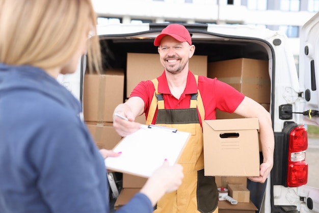 Photo smiling male courier hands over clipboard with pen to woman to sign receipt of parcel