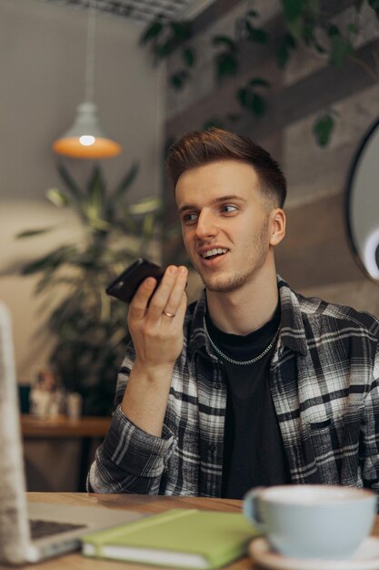 Smiling male freelancer recording voice message on mobile phone while working in restaurant