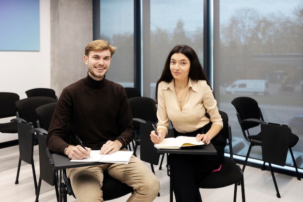 Smiling male and girl sitting on chairs in meeting room Students studying listening to lecture