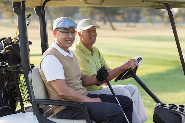 Smiling male golfer friends sitting in golf buggy