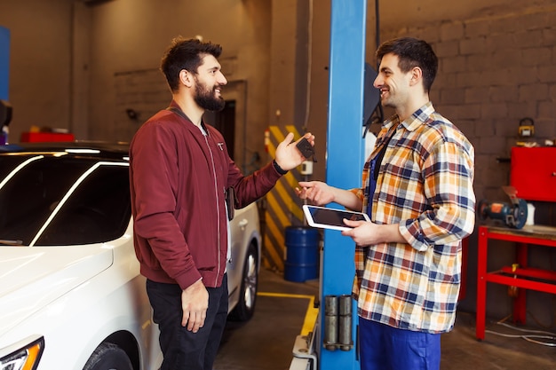 Smiling male repairman holding digital tablet in the hands and talking with customer in the workshop