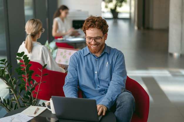 Photo smiling male sales manager in eyeglasses working on laptop sitting in office during working day