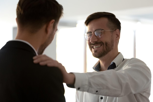 Photo smiling male team leader put hand on colleagues shoulder