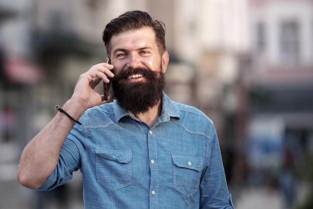 Smiling man call phone and smile outdoor city street Happy businessman in casual blue shirt talking on mobile