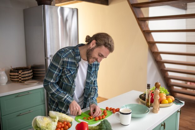 A smiling man cutting cherry tomatoes for a salad