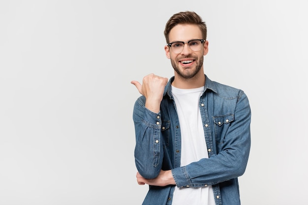 Smiling man in eyeglasses pointing with finger isolated on grey