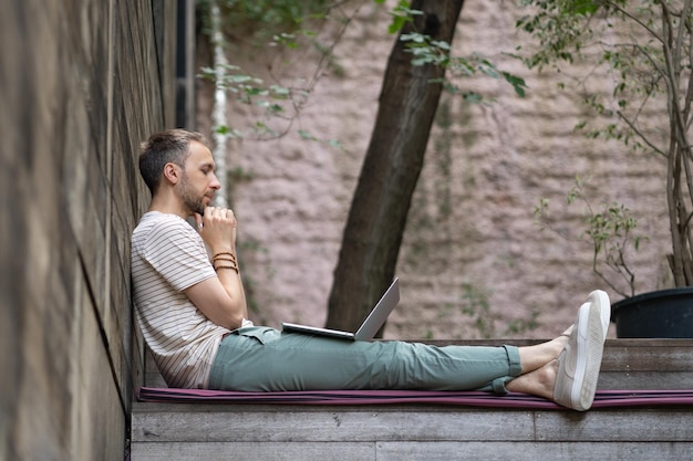 Smiling man freelancer using laptop studying online enjoying distant job working from street