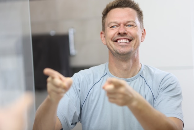 Smiling man in front of mirror points at his reflection.