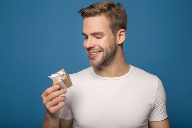 Smiling man holding small gift isolated on blue