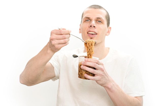 A smiling man holds a fork with fast food noodles in a transparent plastic cup