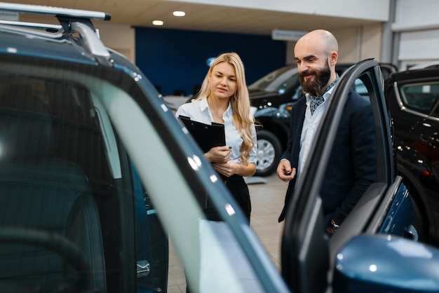 Smiling man and saleswoman in car dealership. Customer and seller in vehicle showroom, male person buying transport, auto dealer business