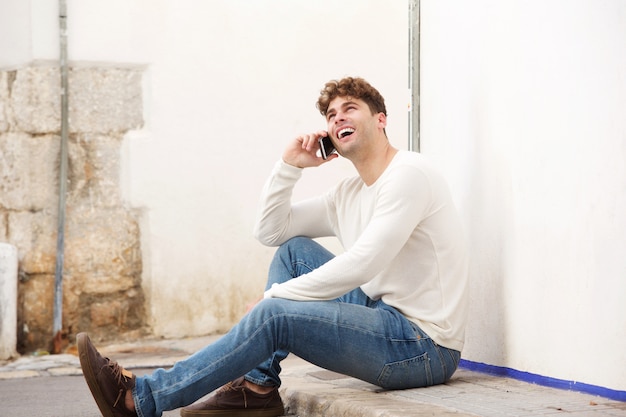 Smiling man sitting on sidewalk talking on mobile phone